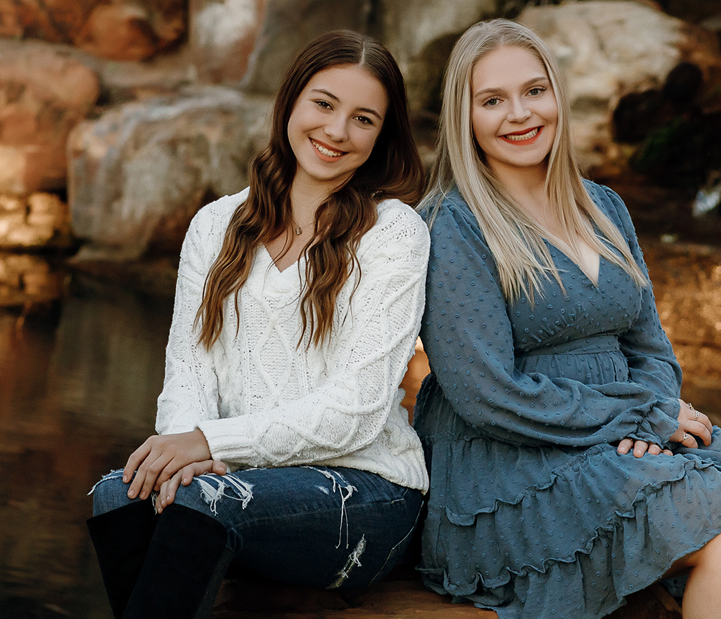 Image of two women sitting and smiling by stone wall | Celebrity Ortho Dentist